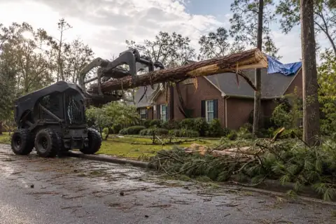 Grapple loader moving storm-broken pine debris from an Alabama residential lot